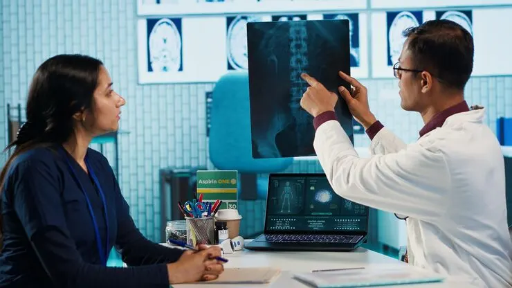 Doctor examining a spinal X-ray while discussing the results with a patient in a medical consultation room.